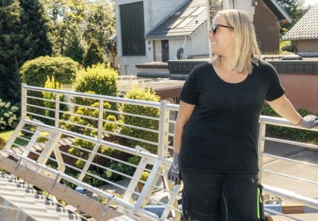 Mitarbeiterin von Schneider Elektrotechnik Sandy lehnt an einem Geländer auf einem Dach - lässig, denn die PV Anlage dort wurde durch eine Förderung finanziert.