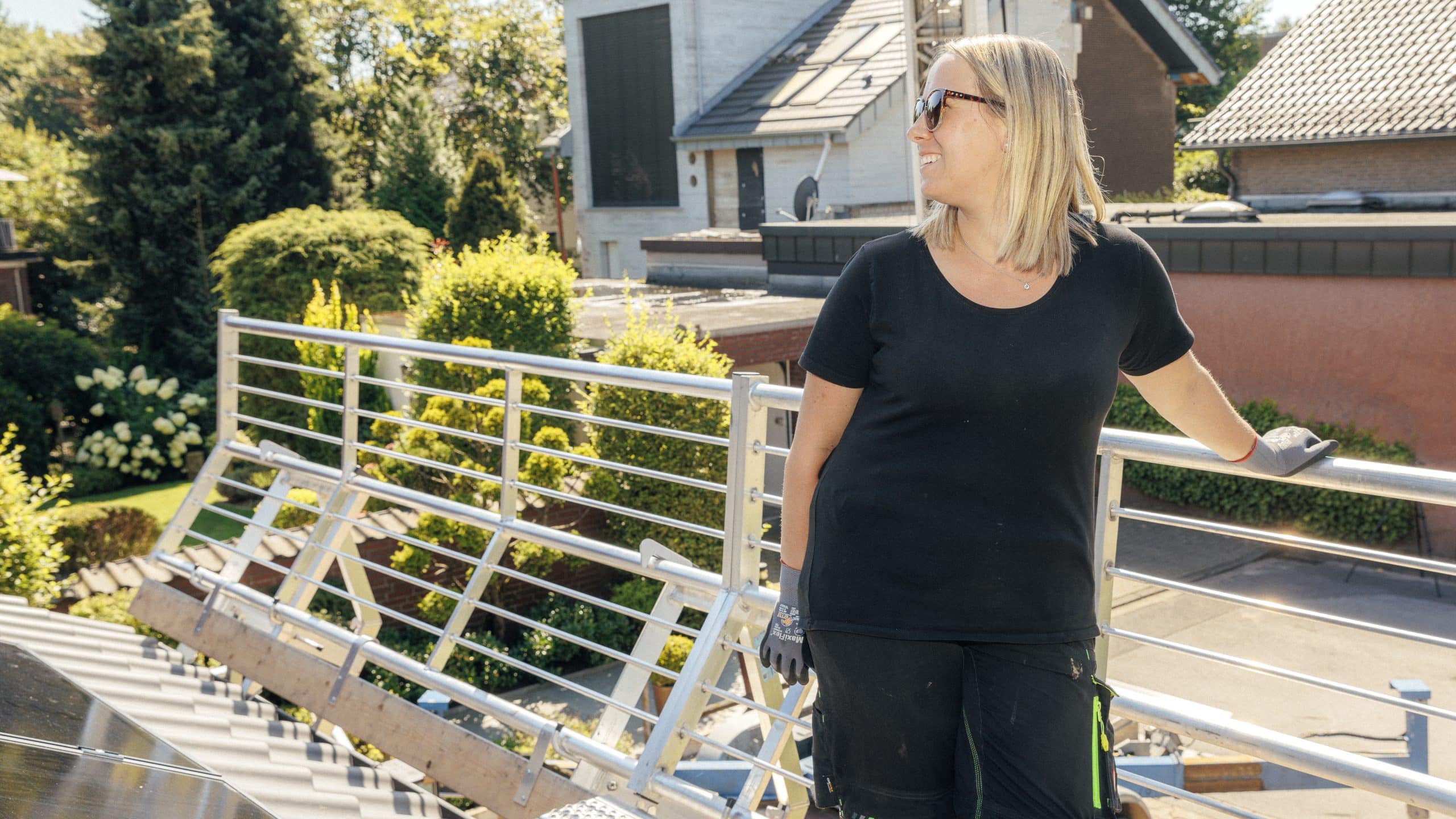 Mitarbeiterin von Schneider Elektrotechnik Sandy lehnt an einem Geländer auf einem Dach - lässig, denn die PV Anlage dort wurde durch eine Förderung finanziert.